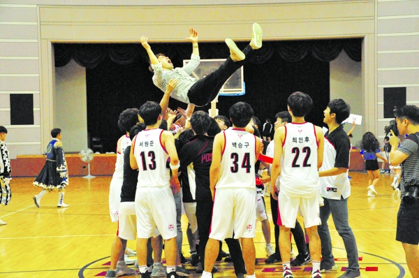 Basketball playerrs tossing their coach in the air after winning the game